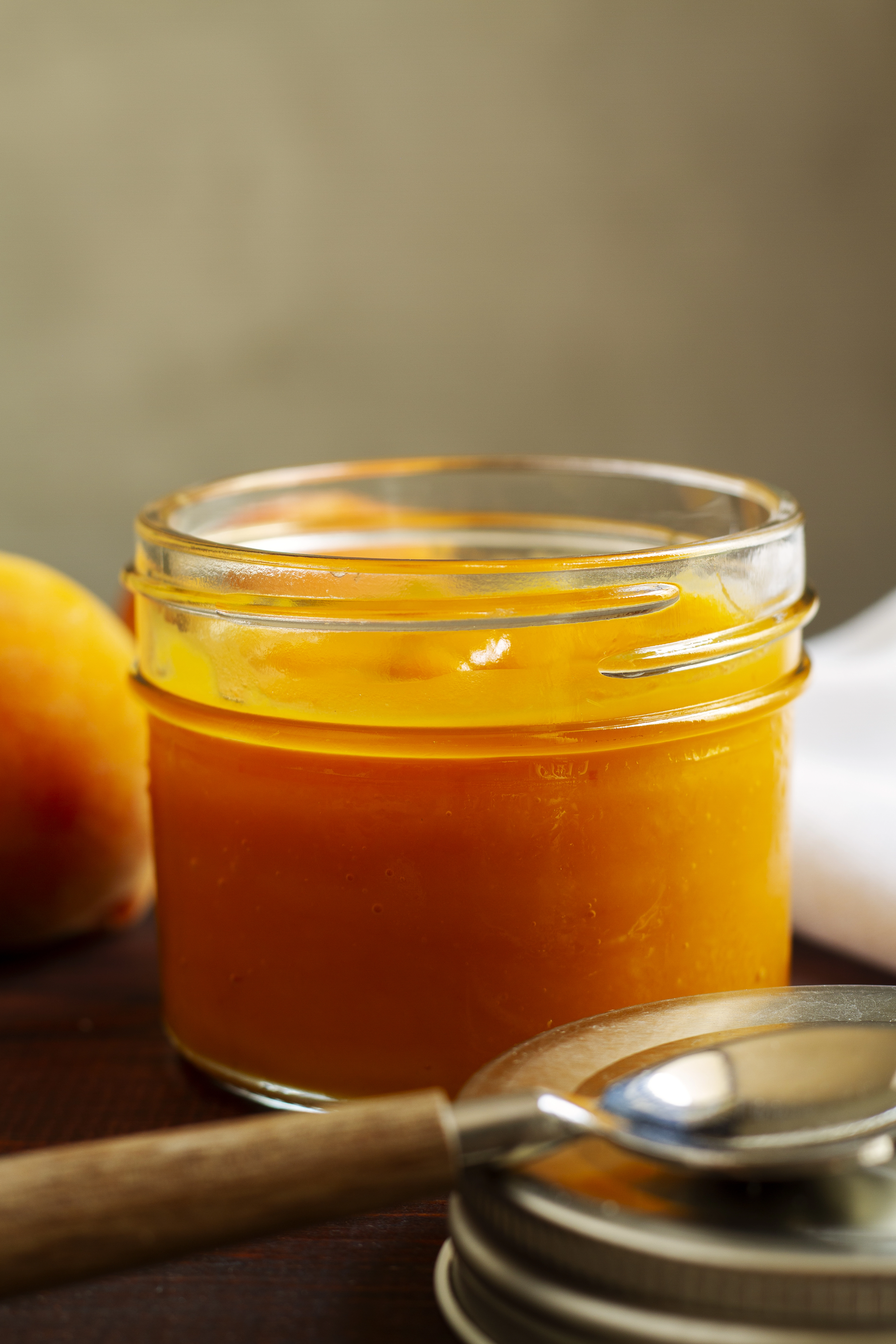 Ein Glas mit frisch gekochter Sanddorn-Marmelade auf Holztisch mit Deckel und Löffel im Vordergrund